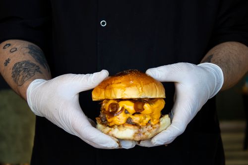 Free A mouthwatering cheeseburger held by gloved hands, showcasing melty cheese and juicy beef patty. Stock Photo