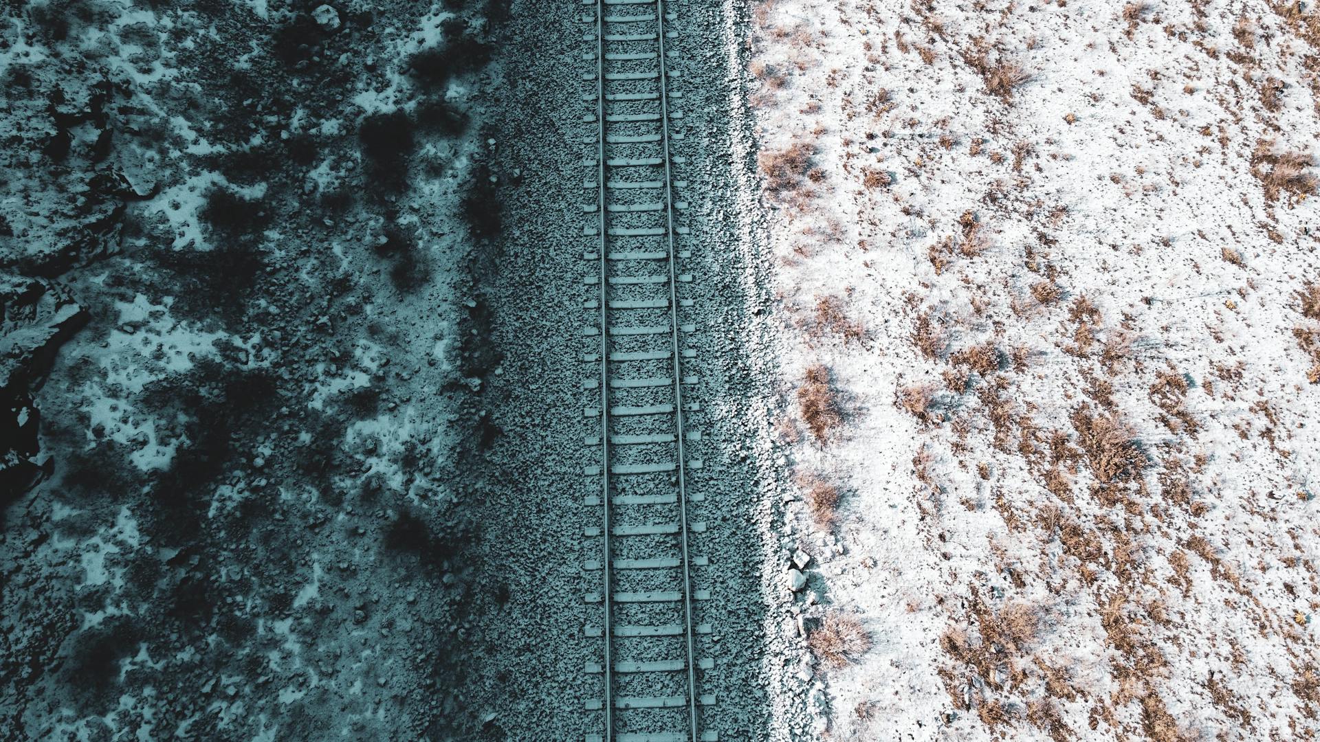 Aerial shot capturing a railroad track dividing snowy and rocky terrains from above.