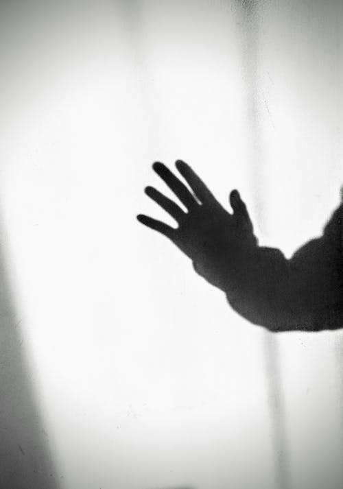 Black and white of shade of anonymous person showing palm of hand in shiny light