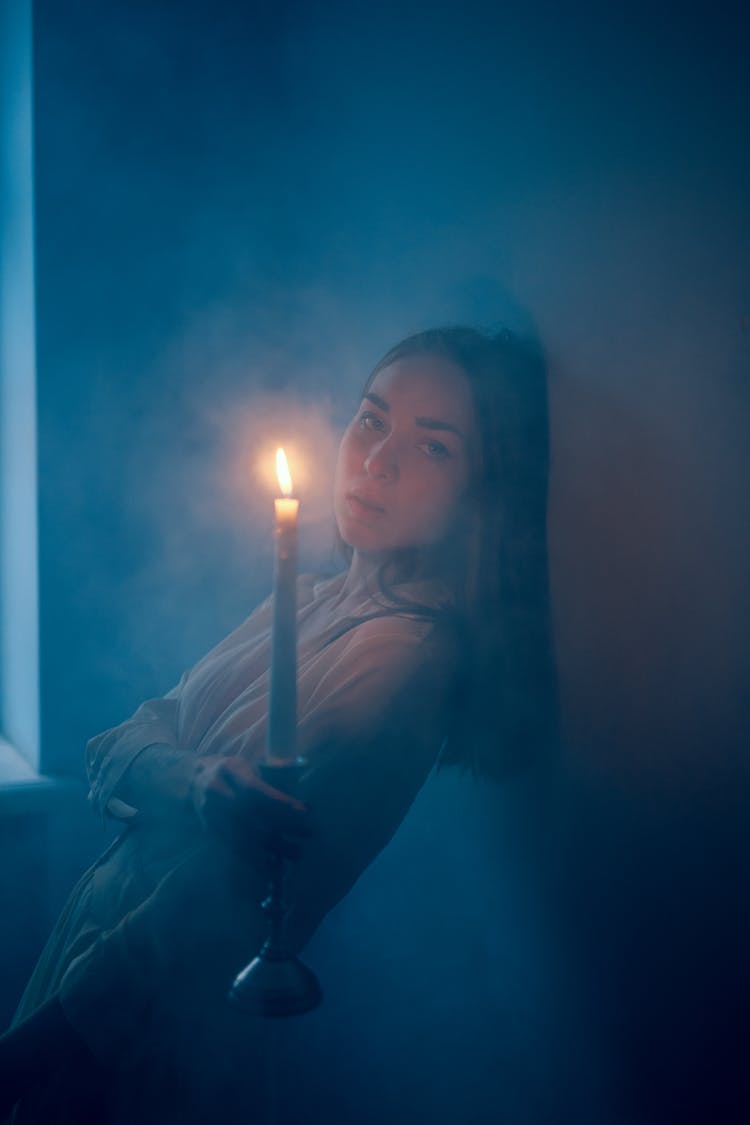 Young Woman With Candle In Dark Room