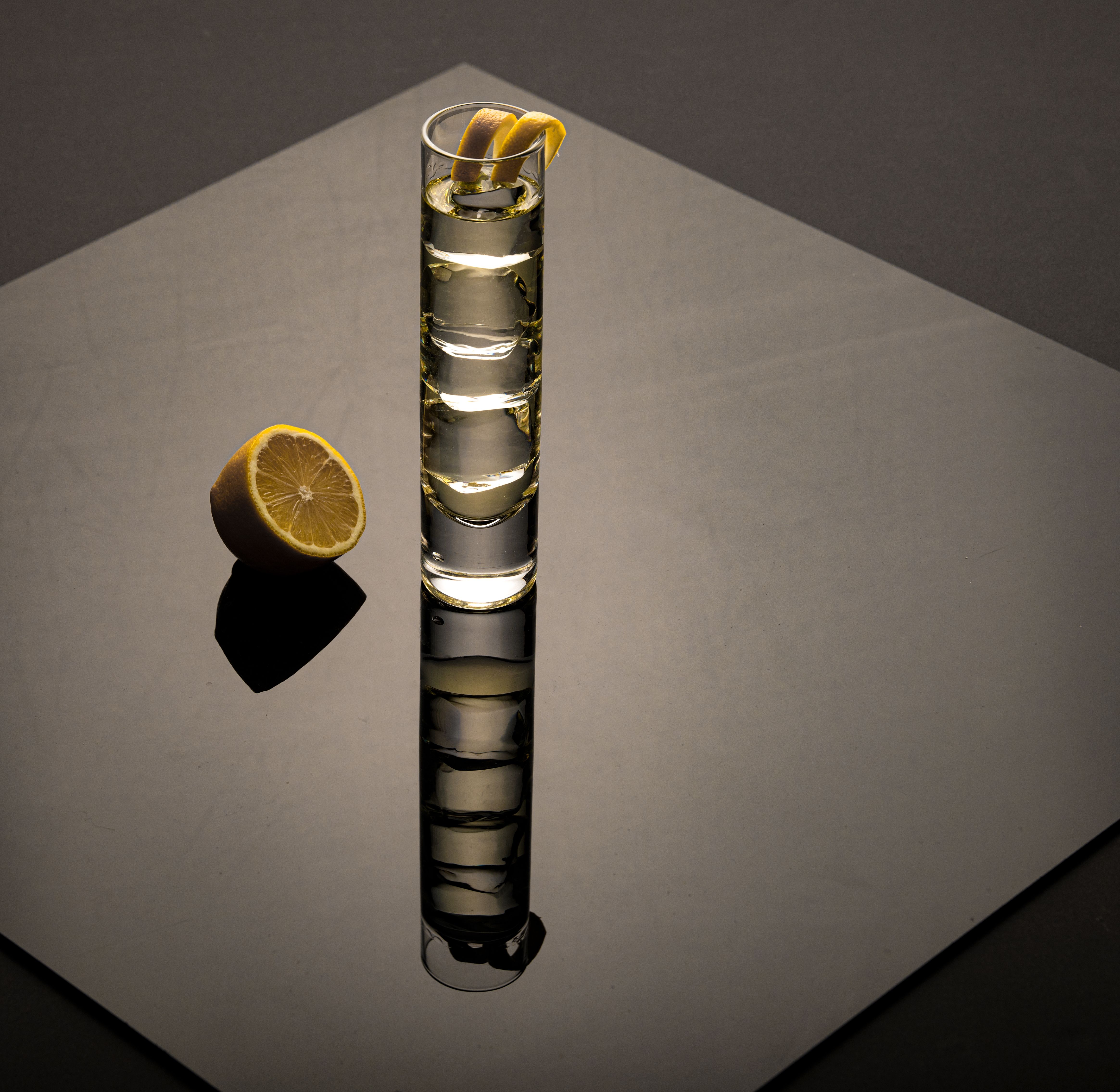 Highball glass with gin and lemon slice on reflective surface.
