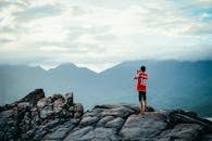 一个人站在岩石山峰上，欣赏着四周郁郁葱葱的风景和广阔的天空