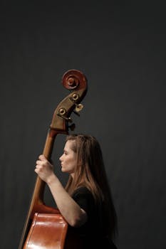 Side profile of a woman playing double bass against a dark studio background.