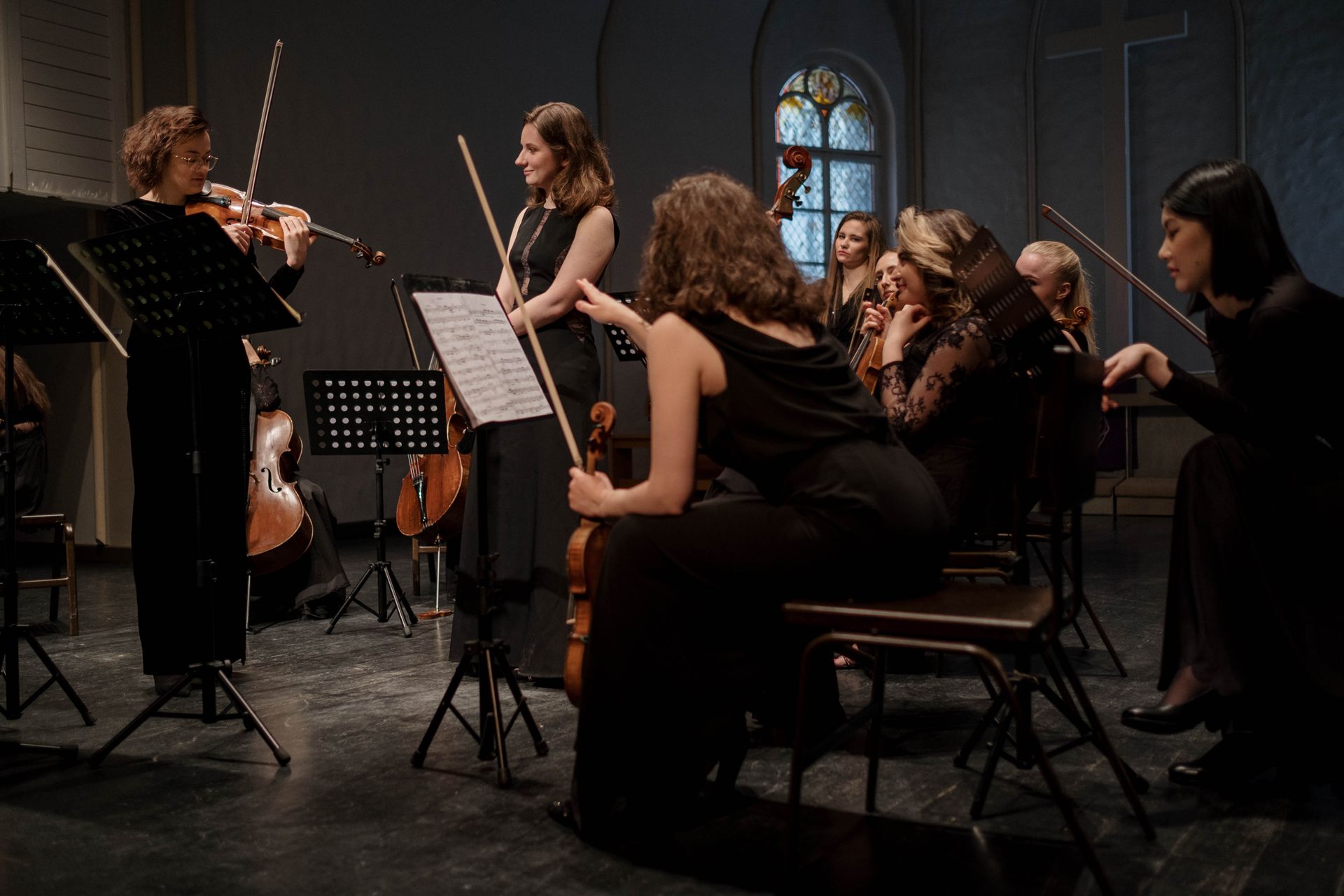 Musicians rehearsing with violins and cellos in a hall; no venue signage visible