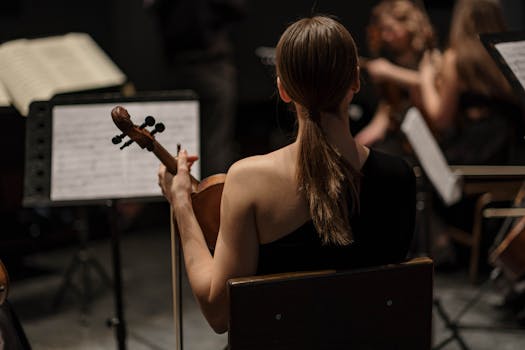 Back view of a female violinist playing in an orchestra setting indoors.