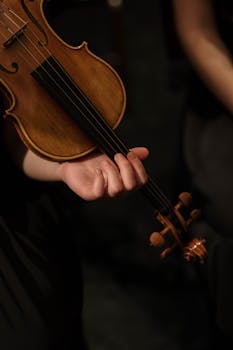 An artistic close-up of a hand holding a violin during a performance.