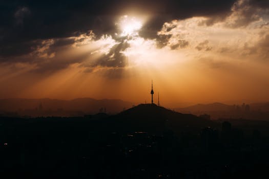 A breathtaking view of the Seoul skyline during golden hour, featuring Namsan Tower silhouetted against dramatic clouds.