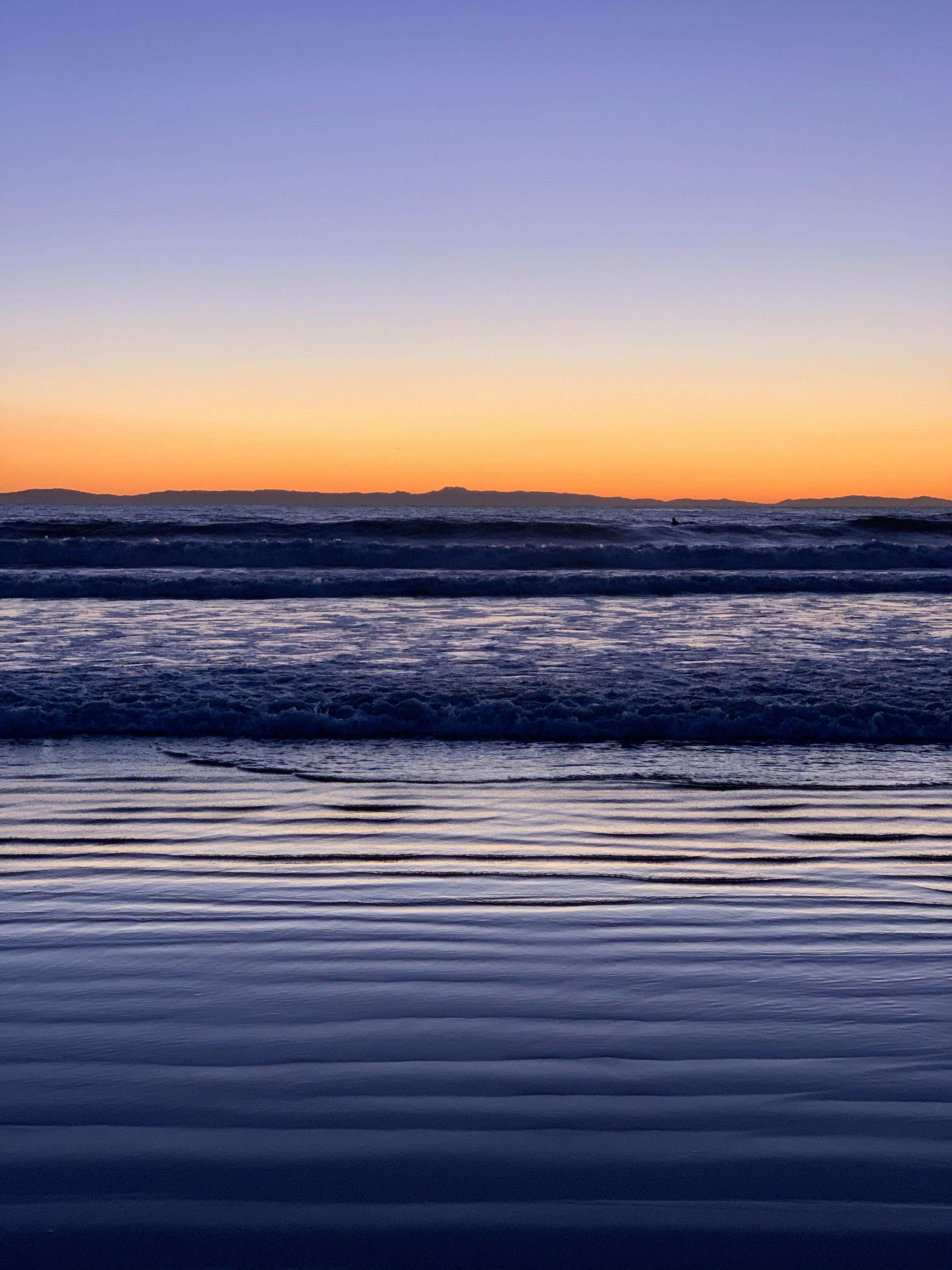 Beautiful sunset over the ocean with gentle waves and vibrant sky colors.