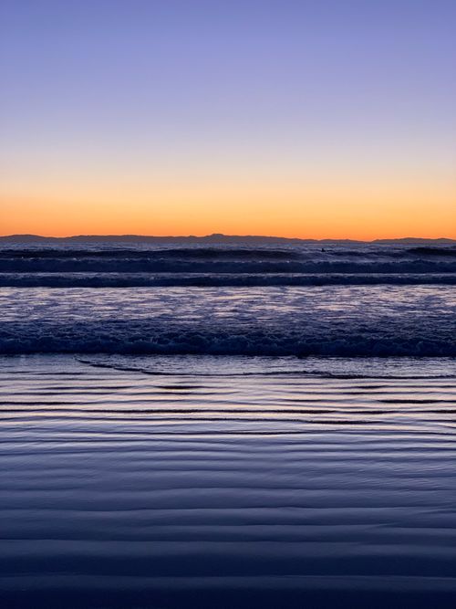 Free Beautiful sunset over the ocean with gentle waves and vibrant sky colors. Stock Photo