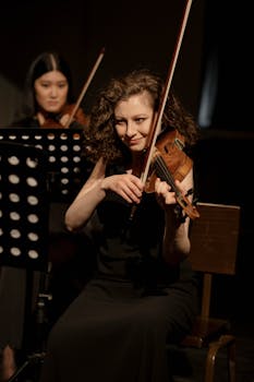 Two women joyfully playing violins during a classical concert, focusing on their expressions and musical instruments.