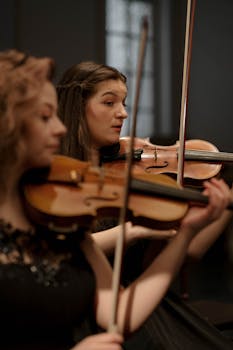 Two women performing classical music with violins, focused and professional.