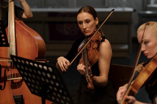 A young female violinist playing passionately in an indoor symphony concert setting.