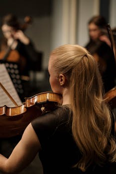 A woman plays the violin in an orchestra setting using a violin bow.