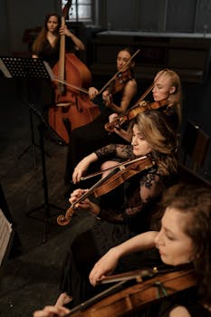 A female orchestra ensemble performing with string instruments in a dimly lit indoor setting.