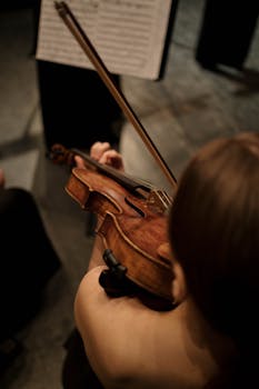 A female violinist playing the violin with sheet music in the background.