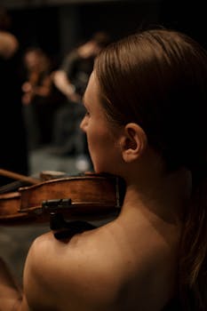 A woman violinist plays passionately during a classical concert, back view.