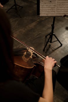 Close-up of a cellist playing on stage, focusing on hand and instrument with visible sheet music.