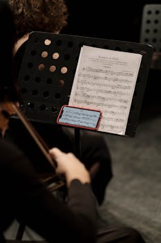 Musician playing a bowed string instrument while reading sheet music during a concert.