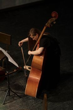 A woman performs a musical piece on a double bass in an indoor concert hall setting.