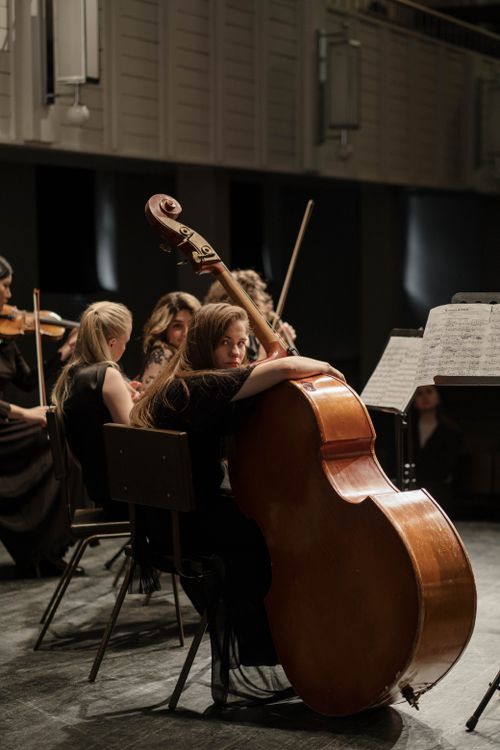 Free Woman playing cello in an orchestral performance in a concert hall setting. Stock Photo
