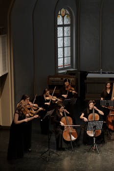 An all-female orchestra performing with violins and cellos indoors on stage.