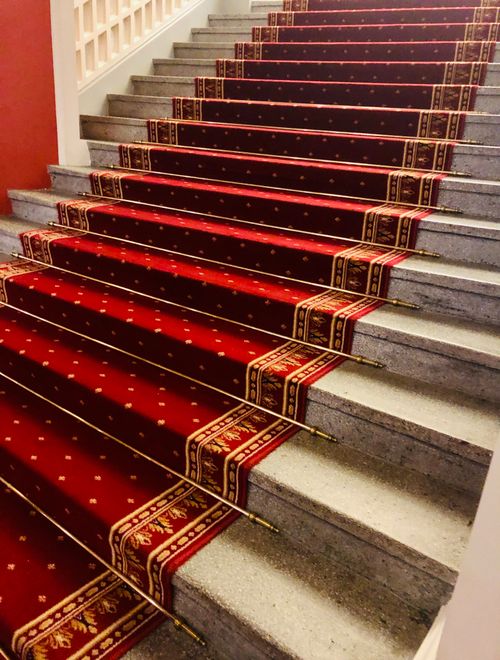 Free A luxurious staircase adorned with a rich, red carpet featuring intricate golden patterns. Stock Photo