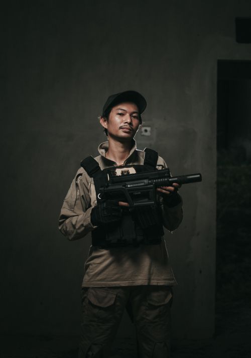 Free An Asian man in military attire holding a firearm indoors, exuding a serious demeanor. Stock Photo