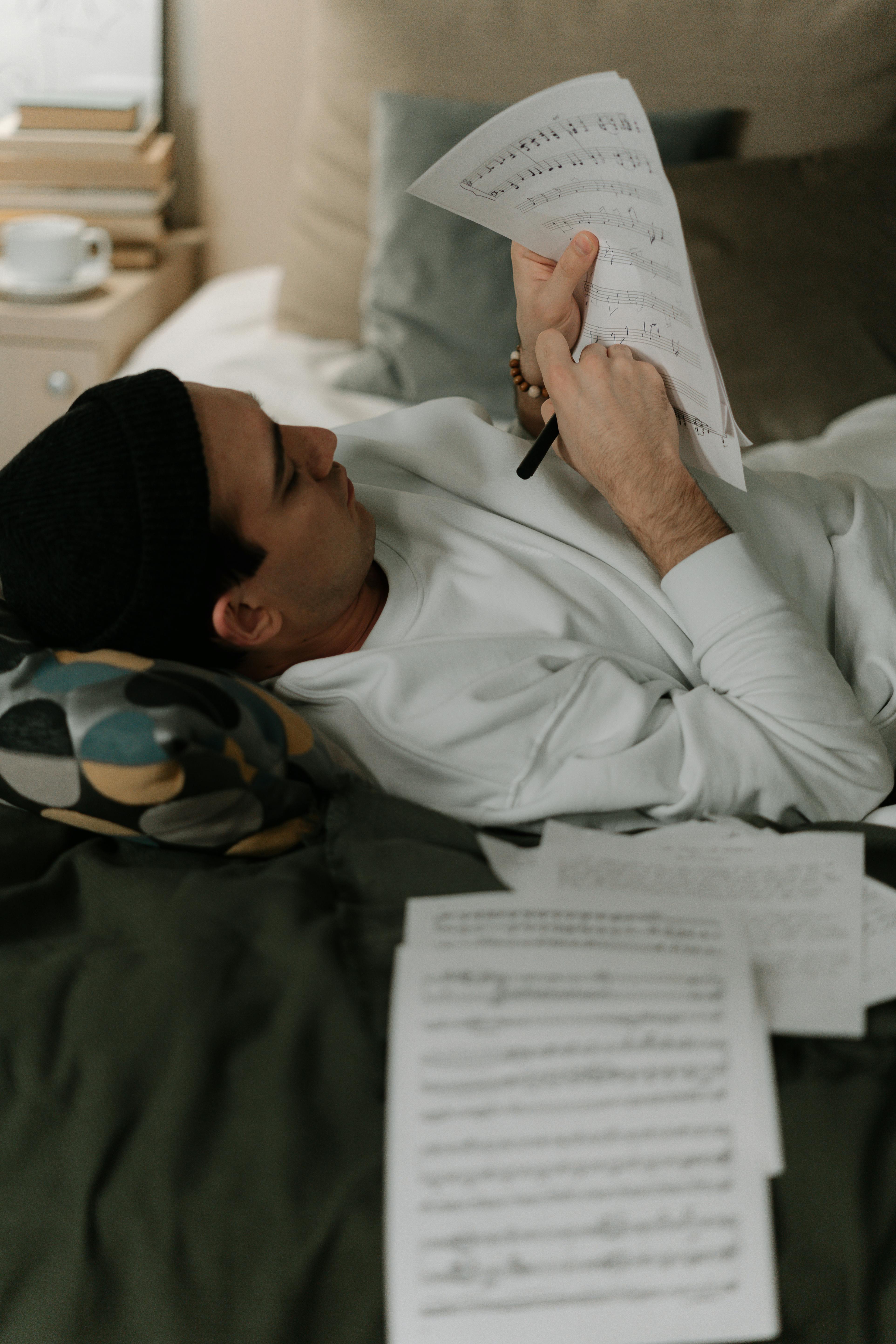 Man lying down indoors, focused on reading musical sheets. Creative and relaxed atmosphere.