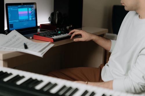 Free A person working on music production using a MIDI keyboard and laptop in a home studio. Stock Photo