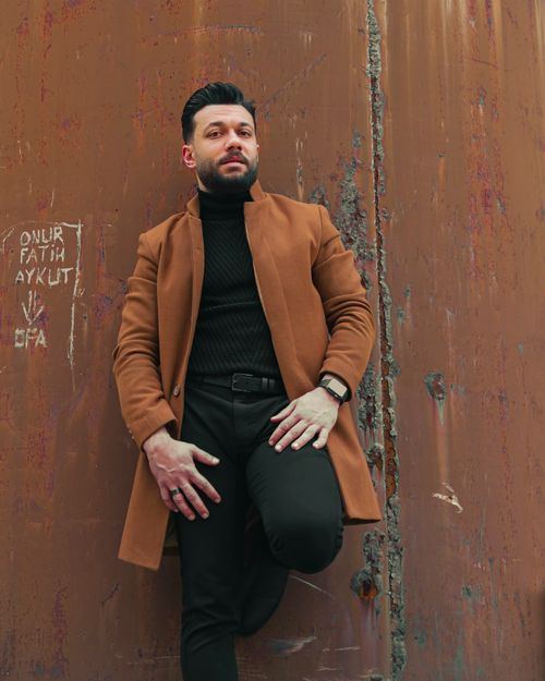 Free Fashionable man in a brown coat leaning against a rustic wall, showcasing elegance and style. Stock Photo