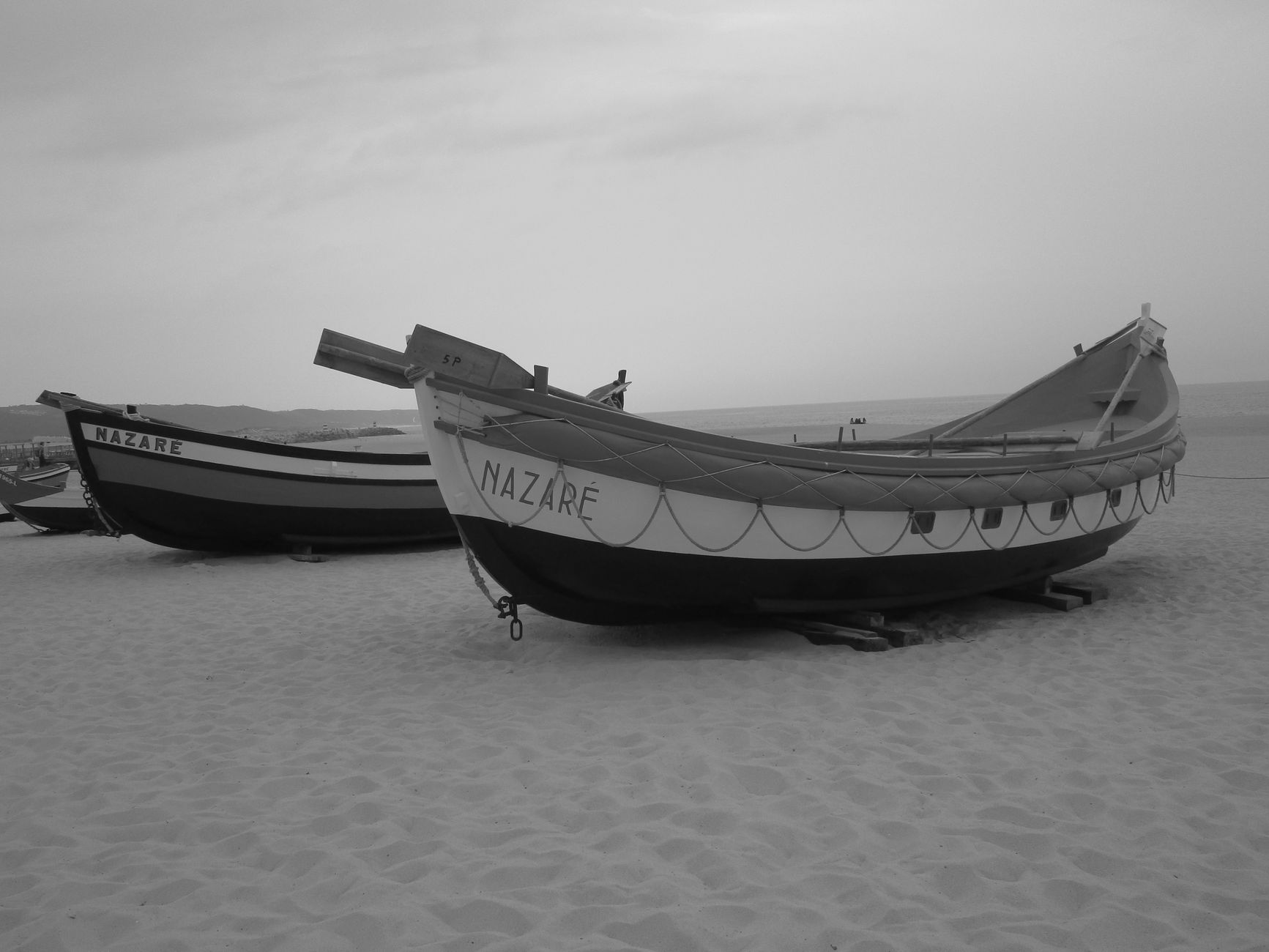 Black and white photo of traditional fishing boats on Nazaré beach, Portugal.