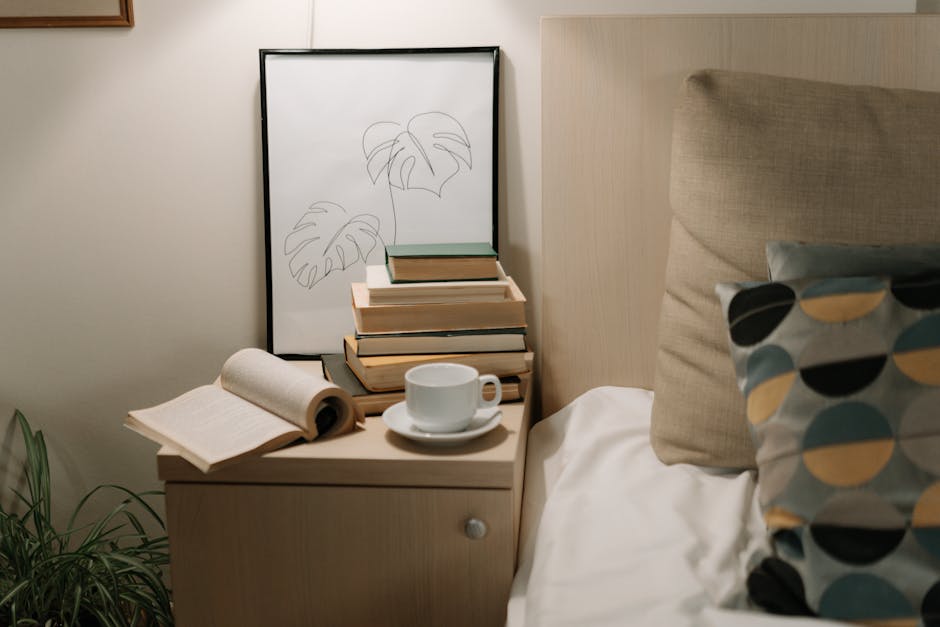 A cozy bedroom with a bedside table, books, and a cup of coffee, perfect for a relaxing day.