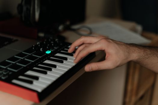 A hand playing a MIDI keyboard in a home studio setting, capturing musical creativity.