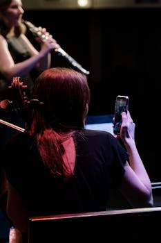 A cellist captures a moment on her phone during a music rehearsal with a flutist.