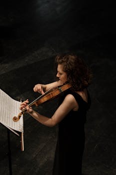 A woman violinist performs with music sheet visible, captured from above.