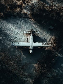 Drone shot of a snow-covered, abandoned airplane nestled in a Latvian forest, captured in winter.