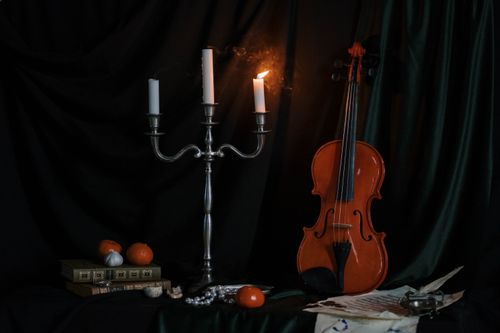 Free A classic still life featuring a violin, candelabra, books, and fruits with moody candlelight. Stock Photo