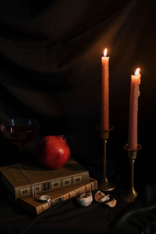 Free A dark and moody still life featuring candles, a pomegranate, books, and more for an artistic touch. Stock Photo
