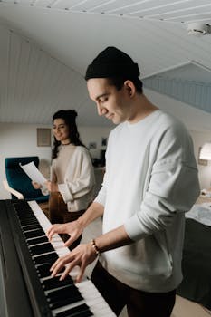 Two musicians composing music together at home, playing keyboard and reviewing sheet music.
