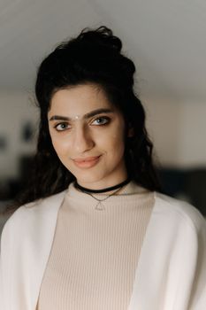A close-up portrait of a smiling woman with dark hair wearing a choker indoors.