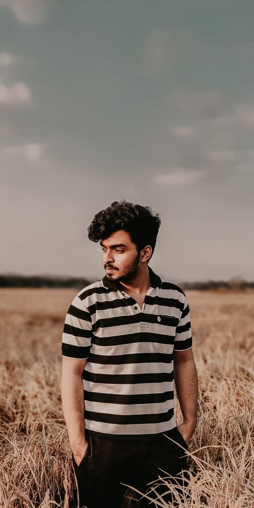 Free A young man in a striped shirt posing thoughtfully in a field during the day. Stock Photo