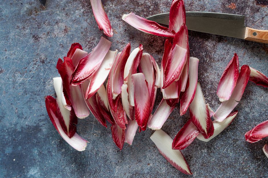 A halved head of radicchio showing its tight magenta and white leaves next to a few loose shredded leaves on a wood board.