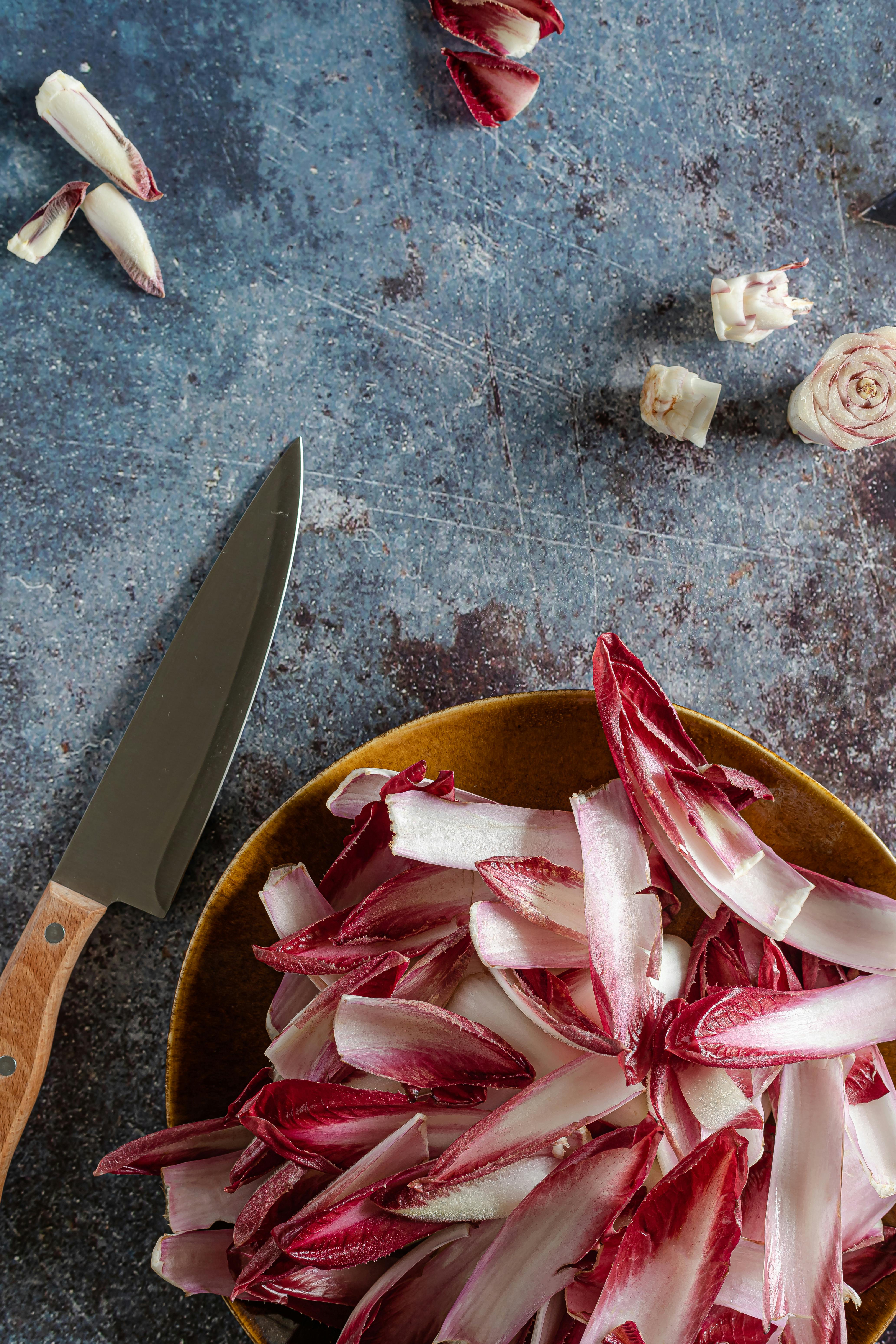 Top view of chicory leaves and a knife on a rustic surface for a fresh salad preparation.