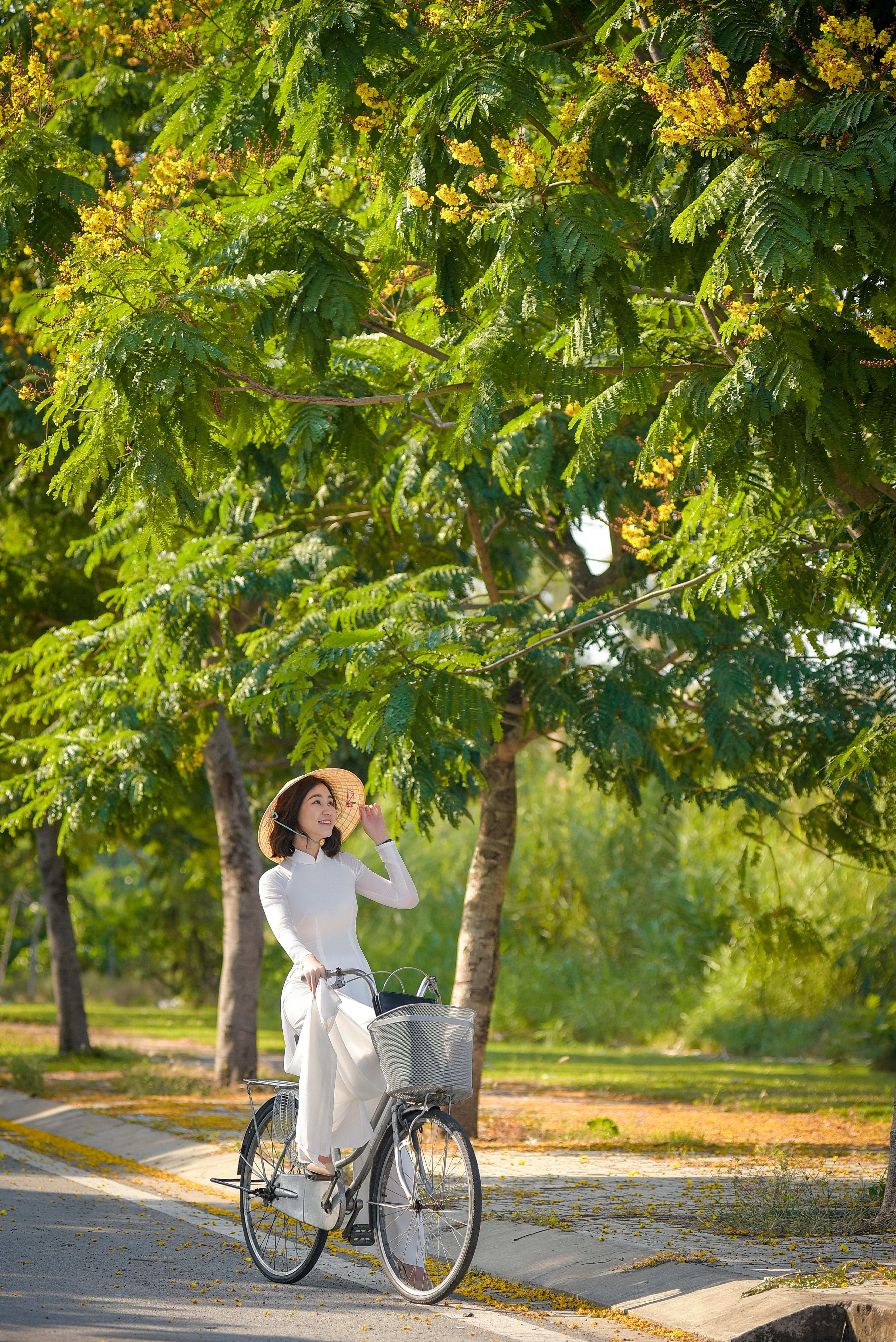 Woman in white dress cycling through a leafy park on a sunny day.