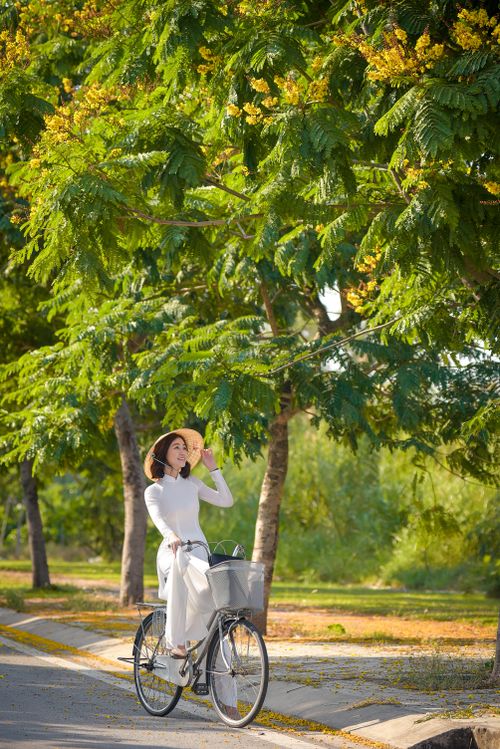 Free Woman in white dress cycling through a leafy park on a sunny day. Stock Photo