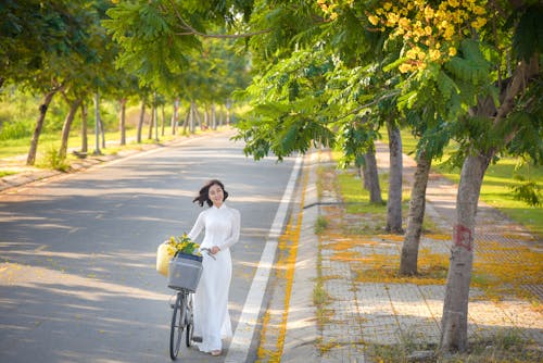 A Woman in White Dress with a Bike Walking on the Road 