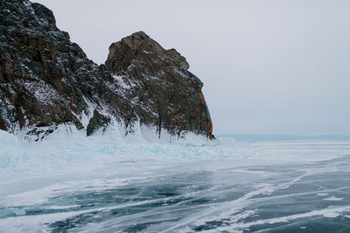 Free A breathtaking scene of icy landscape with towering rocky cliff under a cloudy winter sky. Stock Photo