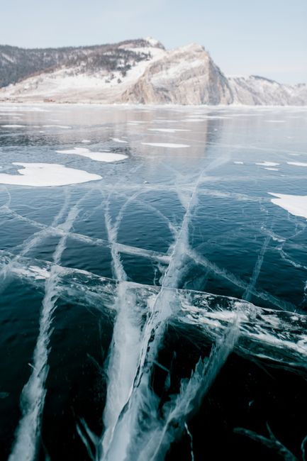 A mesmerizing view of a frozen lake with visible cracks and rugged mountains in the winter scenery.