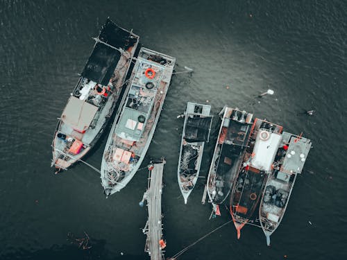Top view of modern fishing boats with nets and fishing tackle moored on pier at seashore