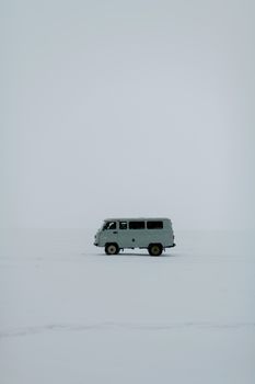 A solitary van traverses a vast snowy expanse in Russia, capturing winter's stark beauty.